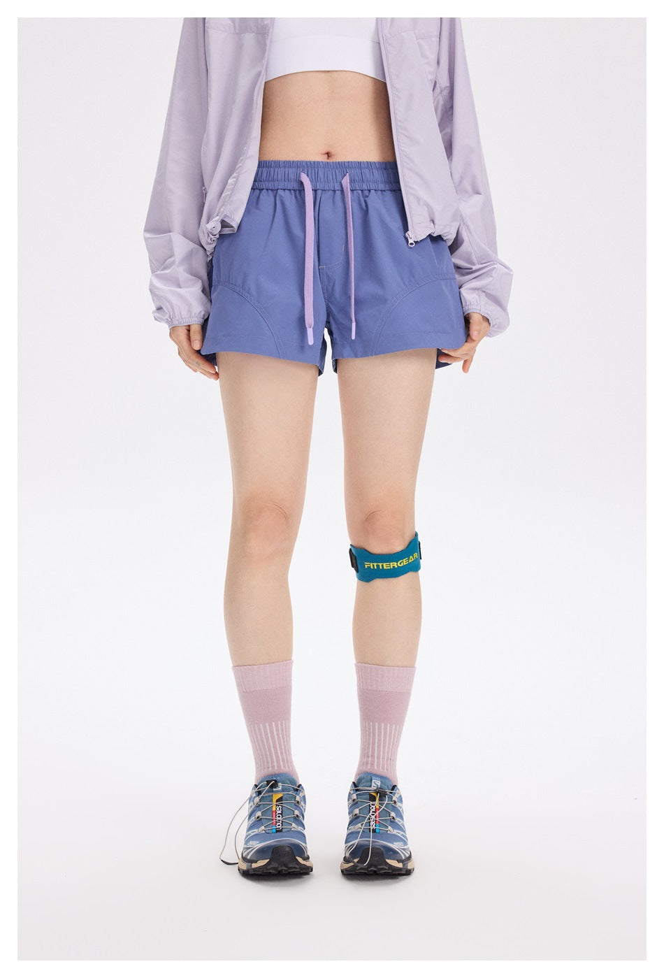 Front view of a model wearing blue-violet running shorts with a lilac drawstring and curved front pockets.