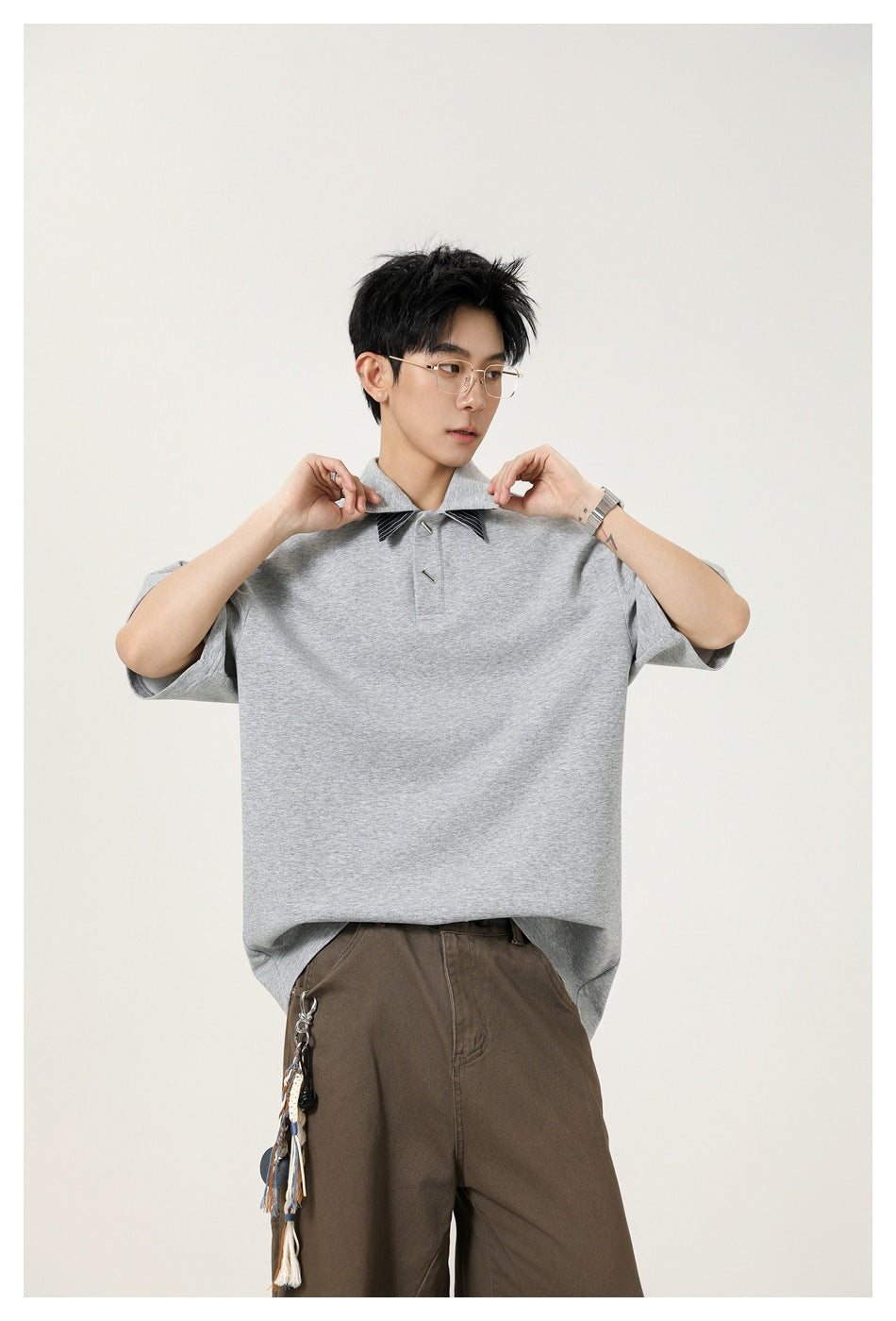 Model adjusting the collar of an oversized light gray short-sleeve polo with dark striped accents.