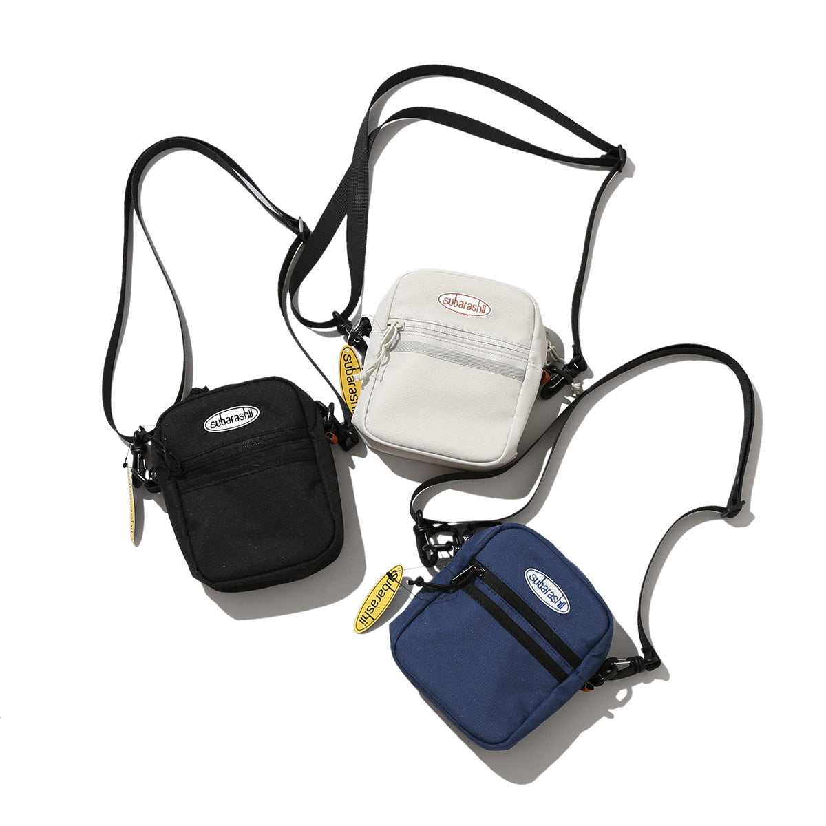 Three small crossbody bags in black, off-white, and navy arranged with their long adjustable straps.