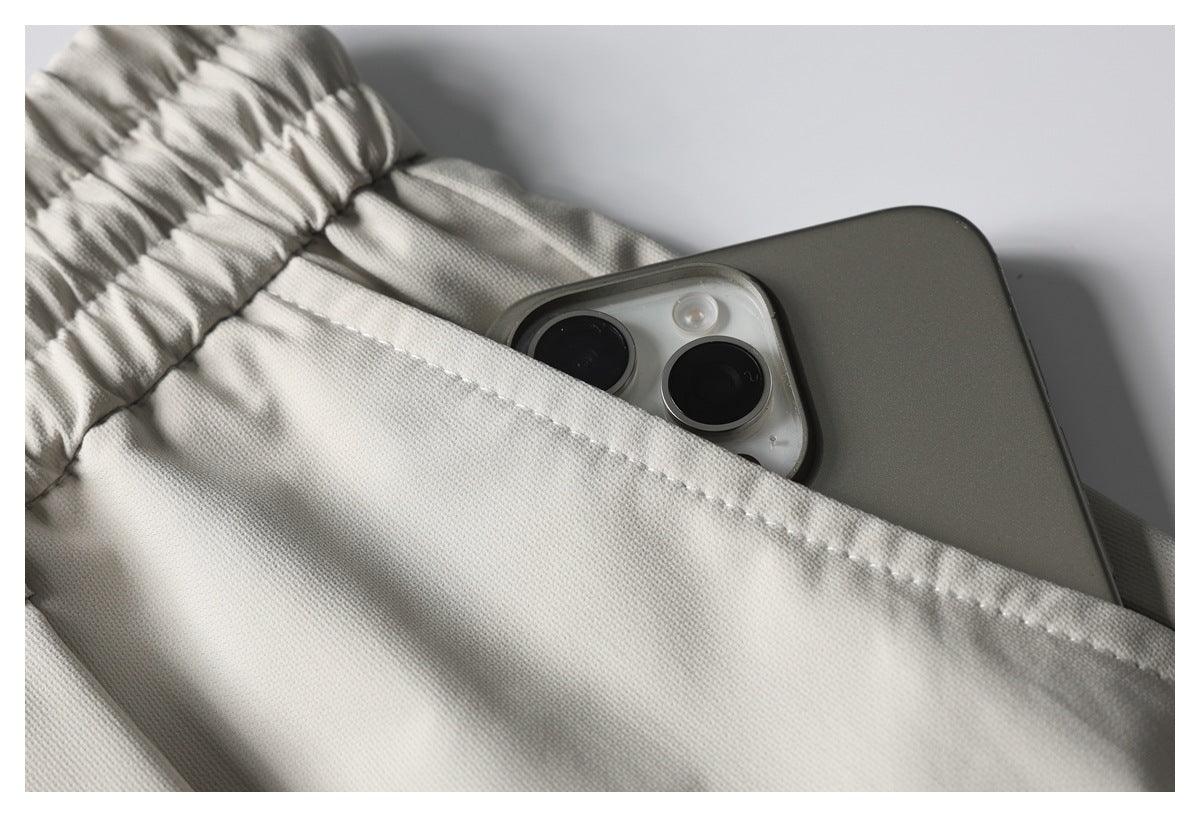 Close-up of a light beige pants pocket with a smartphone tucked inside beneath the elastic waistband.