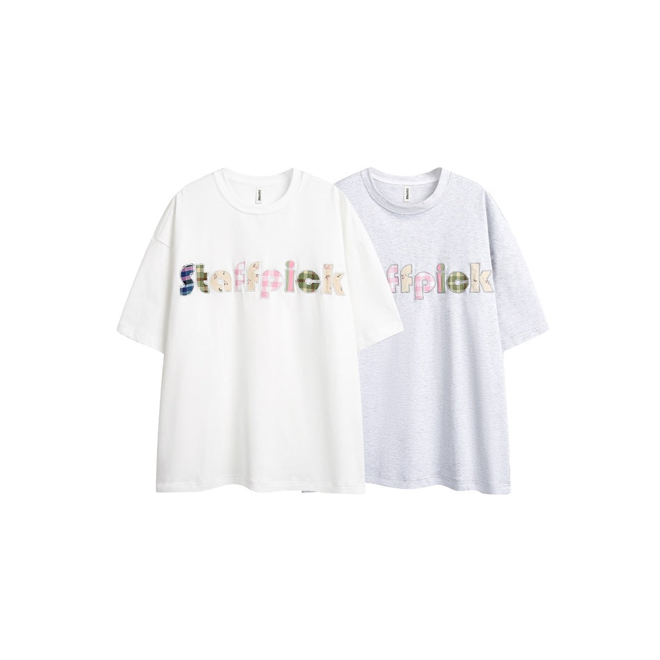 Two oversized T-shirts, one white and one light gray, both with colorful patchwork lettering across the chest.