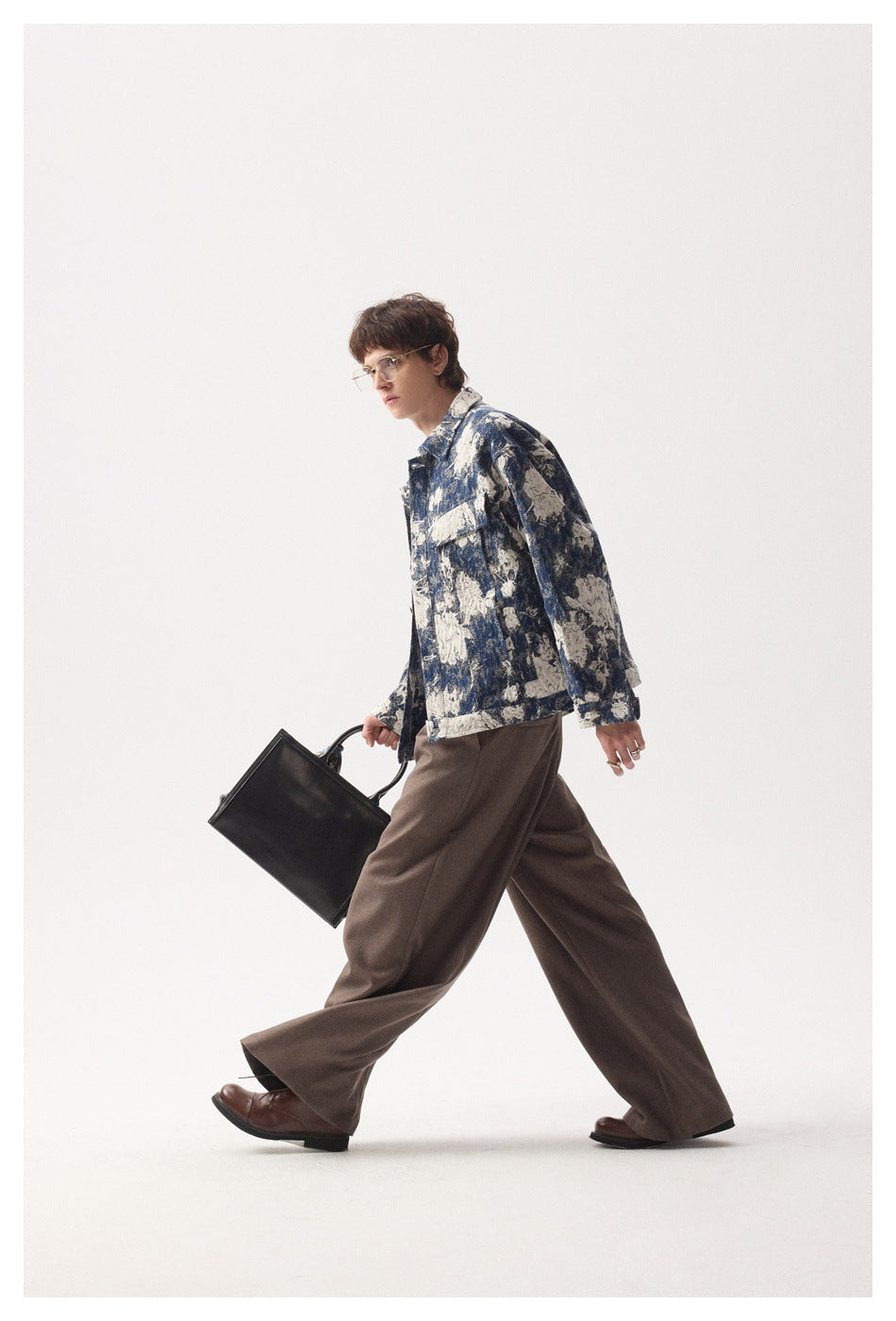 Full-length view of a model walking in a blue and cream floral jacket with wide brown trousers.