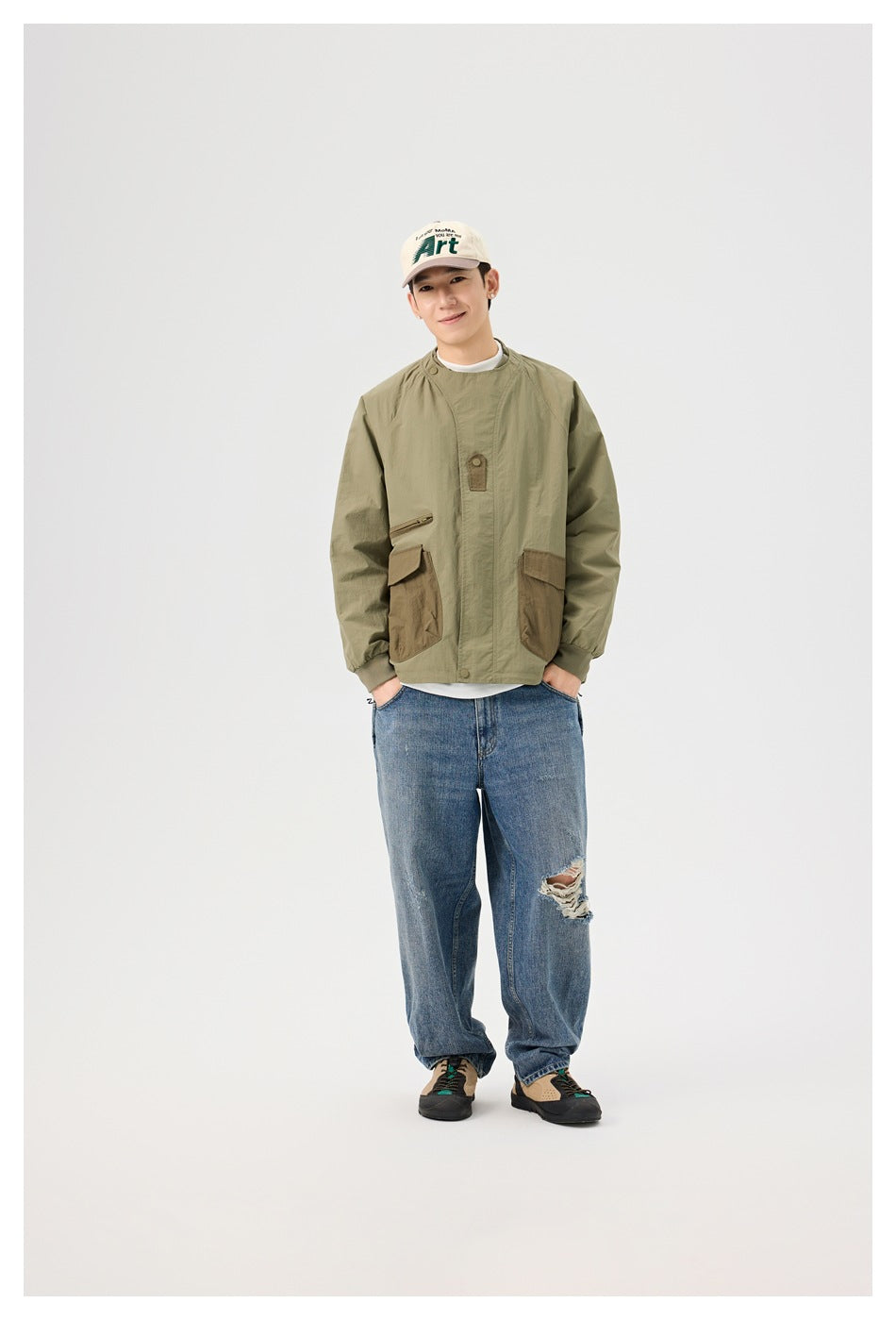 Full-length view of a man wearing an olive jacket with contrasting brown pockets and relaxed blue jeans.