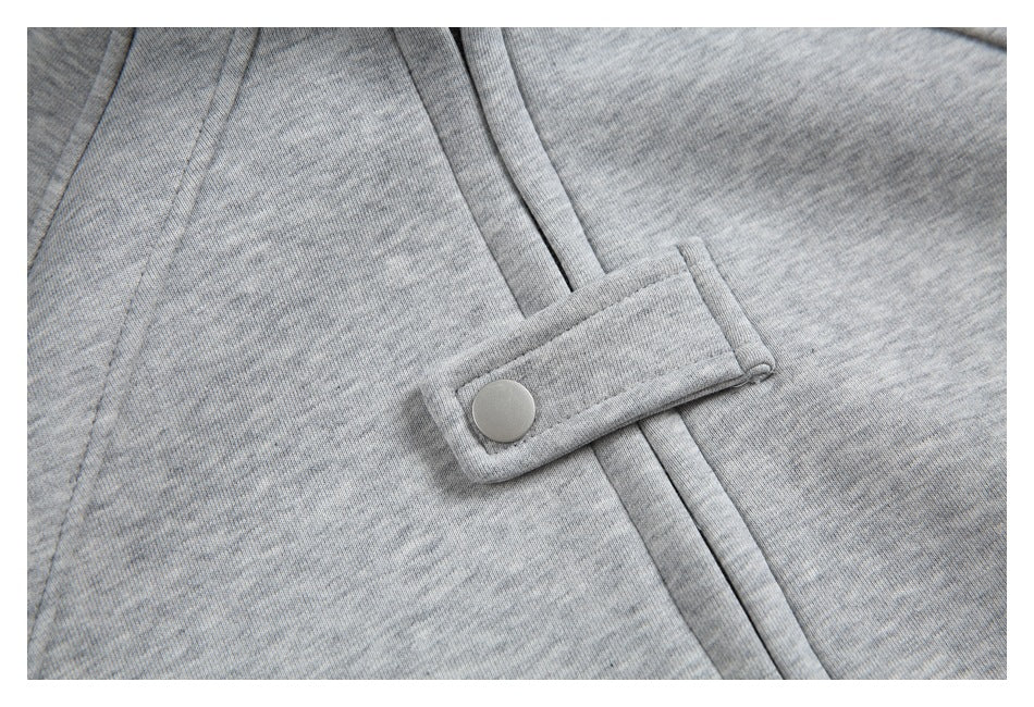 Close-up of a gray heather garment with a snap-button tab crossing a stitched front seam.