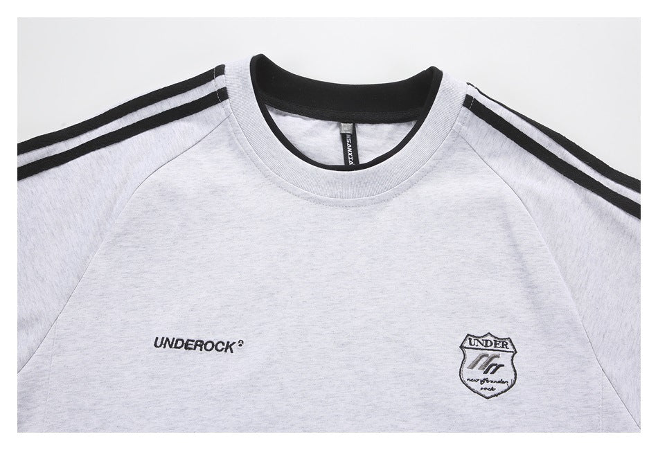 Close-up of a light gray sweatshirt front with a black ribbed crew neck, striped shoulders, and embroidered chest logos.