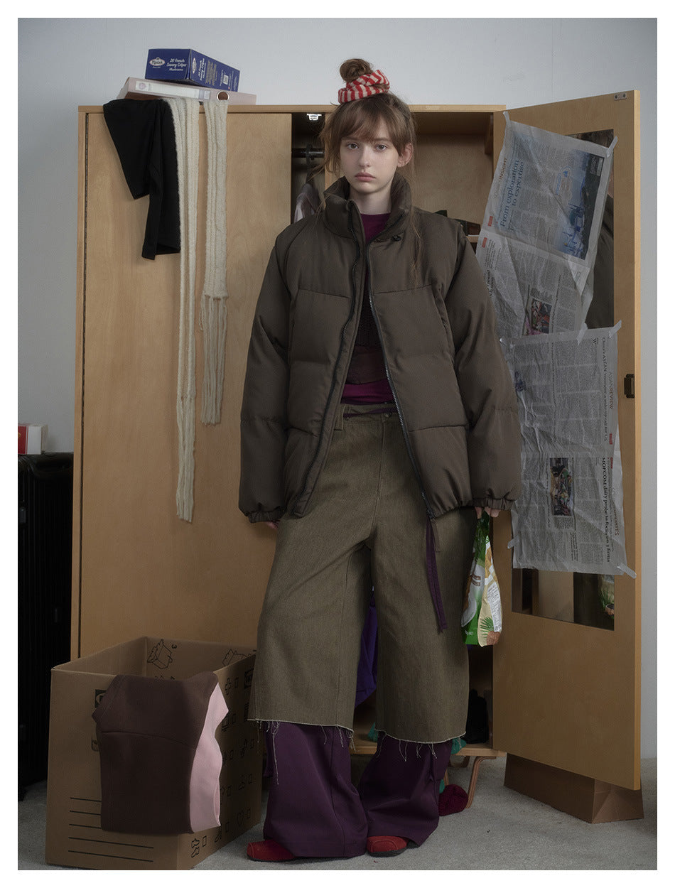 Model wearing an olive-green puffer jacket open over a purple top with olive wide-leg pants in a cluttered wardrobe setting