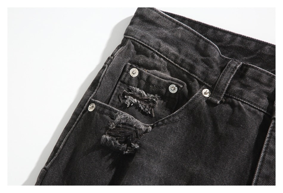 Close-up of black washed jeans showing a front pocket, metal rivets and frayed distressing.