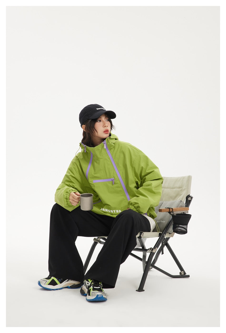 Model seated in a lime-green jacket with lavender zippers and a raised collar, holding a mug.