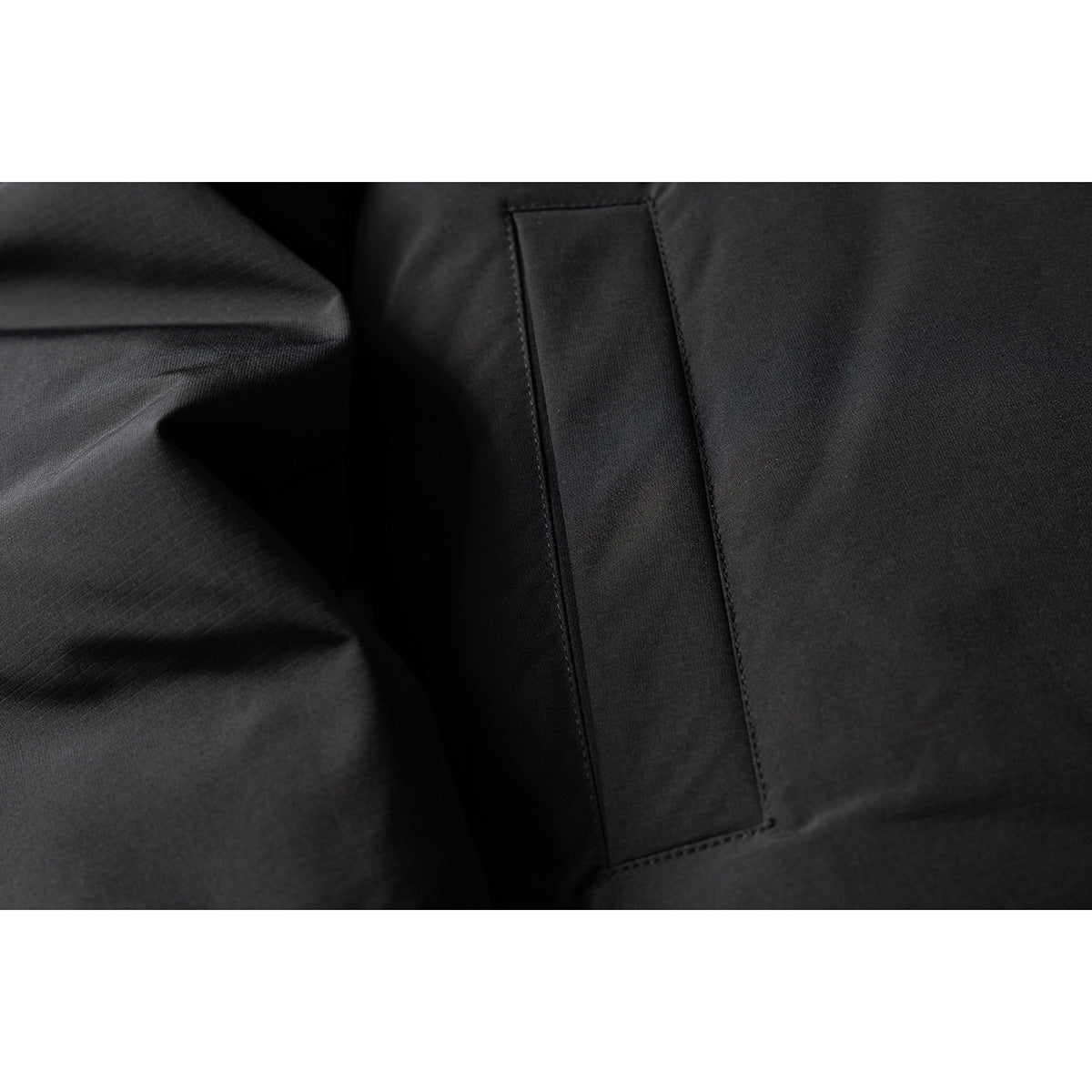 Close-up of a black jacket's stitched rectangular pocket panel and fabric.
