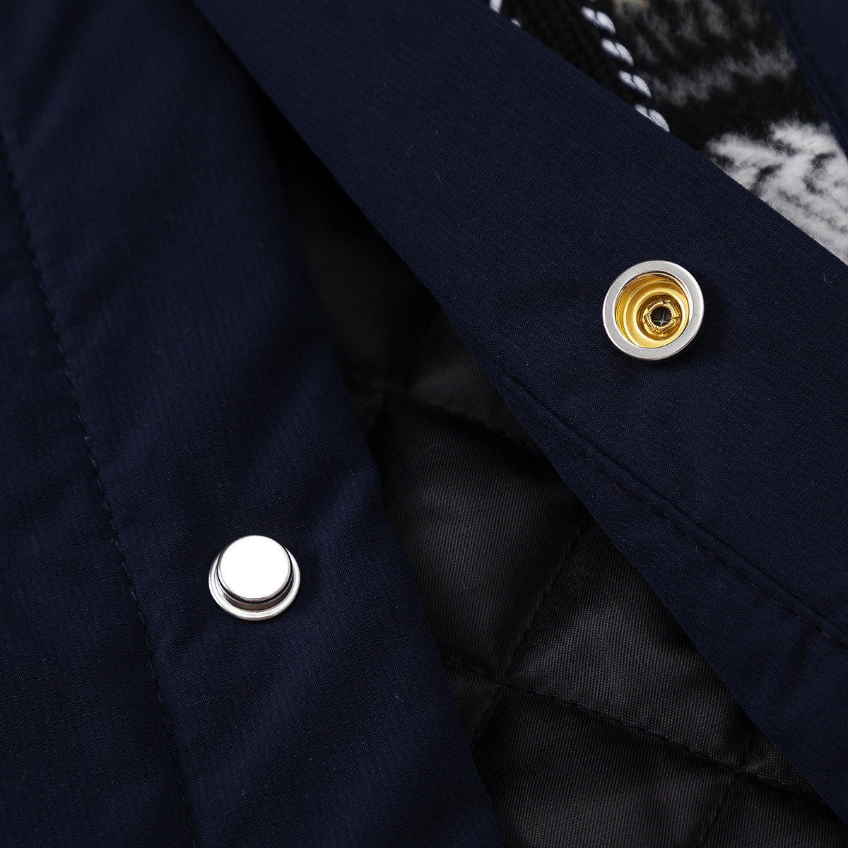 Close-up of silver and gold-tone snap fasteners on navy fabric, with plaid fabric at the edges.