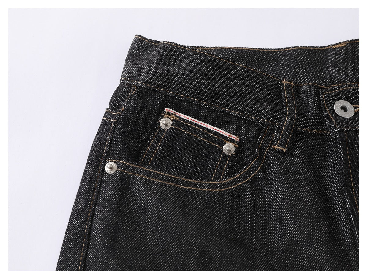 Close-up of black denim jeans showing the front pocket, small coin pocket, rivets and tan contrast stitching.
