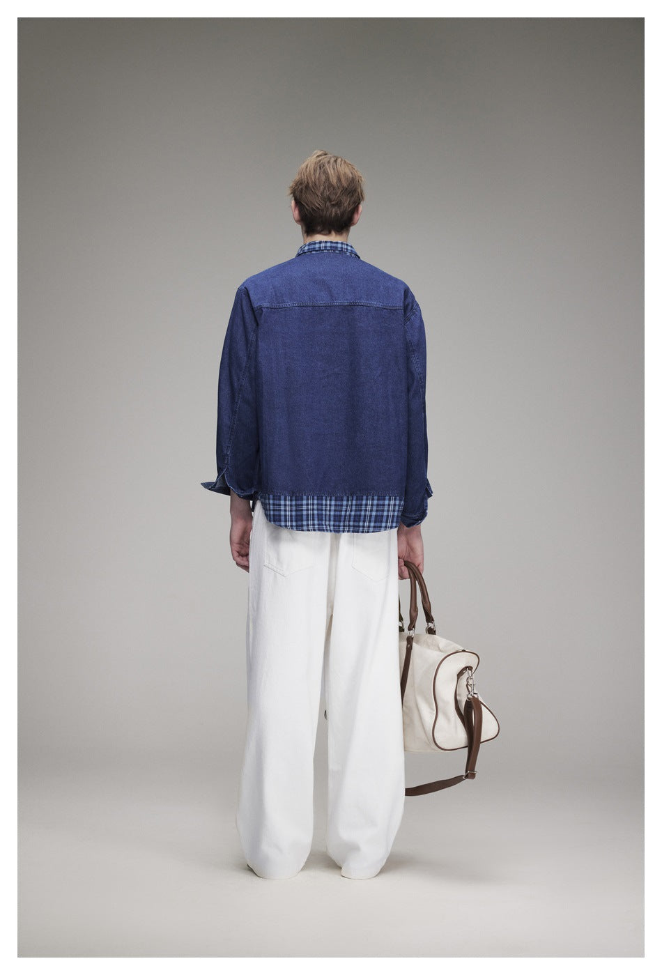 Back view of a model wearing a blue denim overshirt with plaid collar and hem, paired with white trousers.