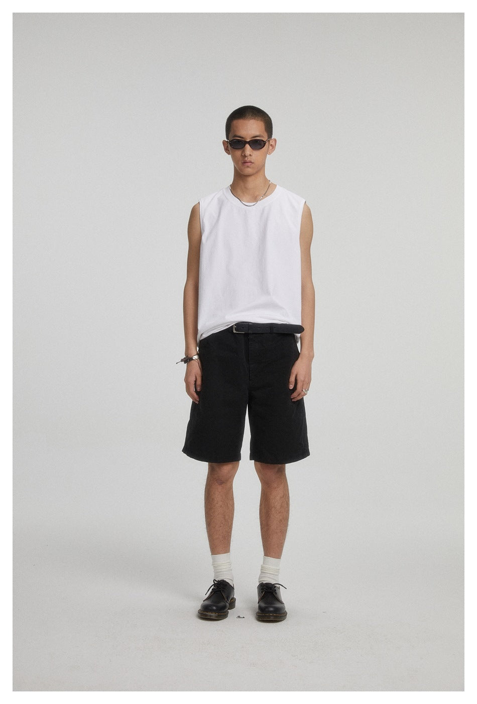 Front view of a model wearing a plain white sleeveless crew-neck top and black shorts.