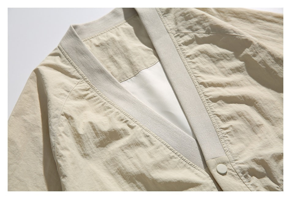 Close-up of the beige jacket’s V-neckline, ribbed trim, shoulder seam, and front snap.
