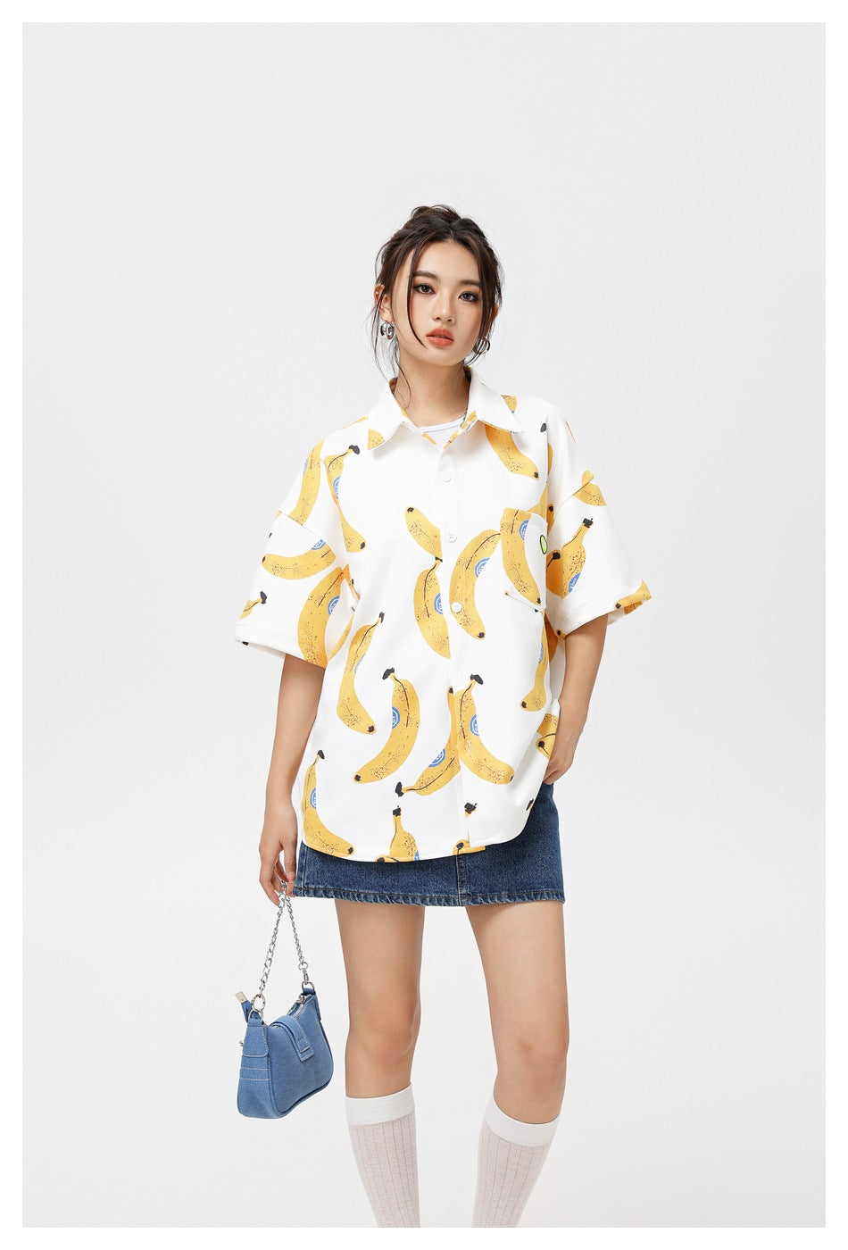 Model wearing a white short-sleeve button-up shirt covered in yellow bananas, paired with a blue denim skirt.