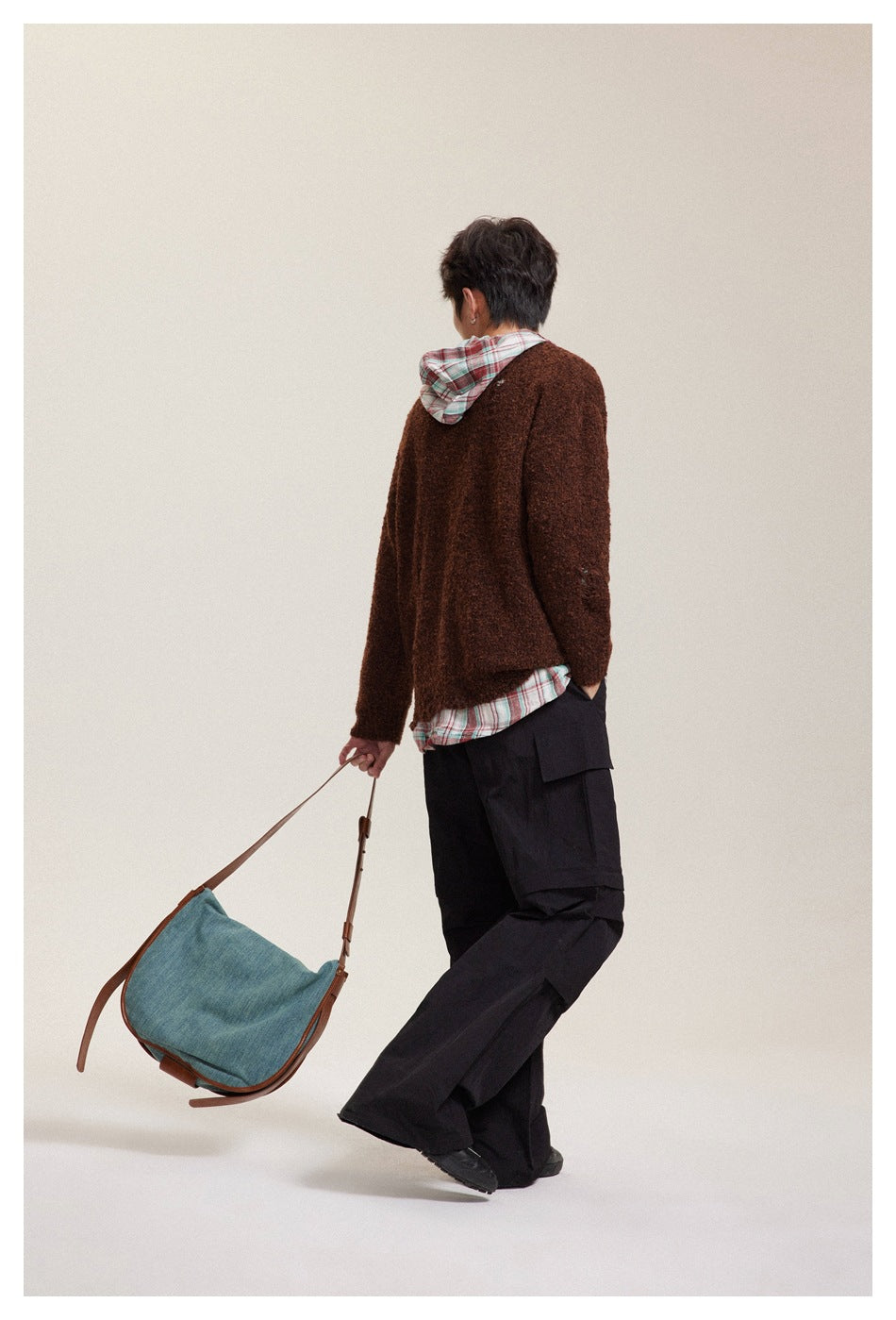 Rear view of a model wearing a brown sweater over a plaid hooded shirt with black cargo trousers.