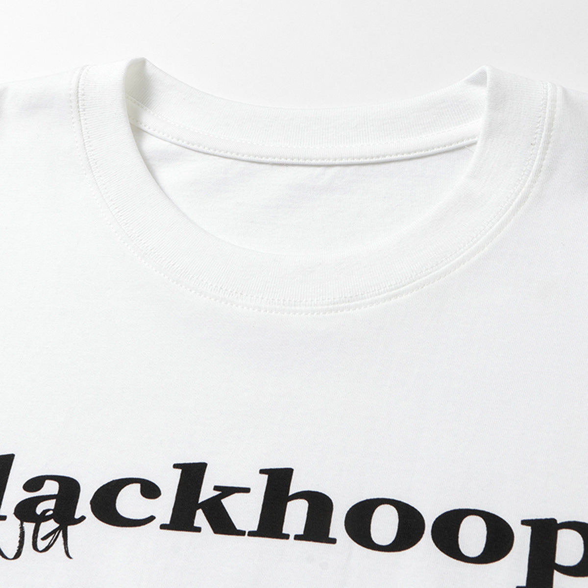 Close-up of a white T-shirt's ribbed crew neck and cropped black chest lettering.