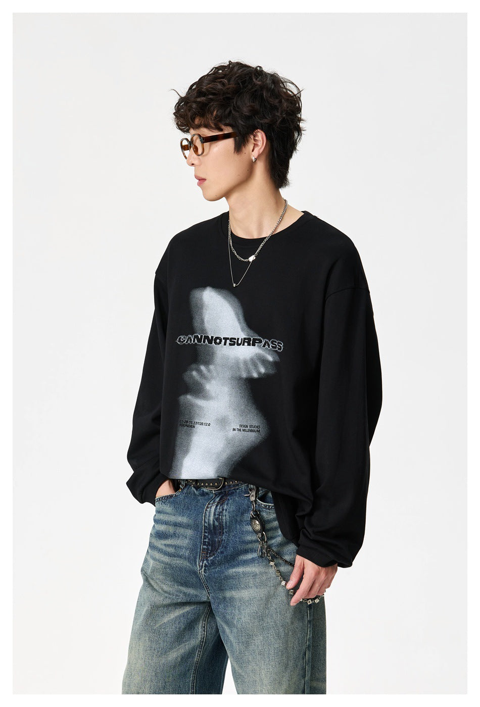 Model wearing a loose black graphic sweatshirt with a grayscale print and wide blue jeans, shown at a three-quarter angle.