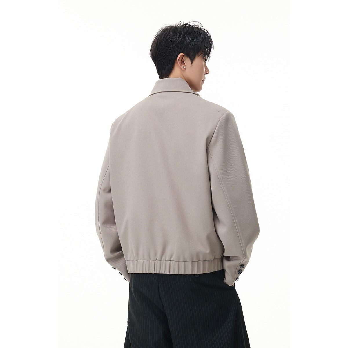 Rear view of a model wearing the taupe jacket, showing its plain back, buttoned cuffs and ribbed hem.