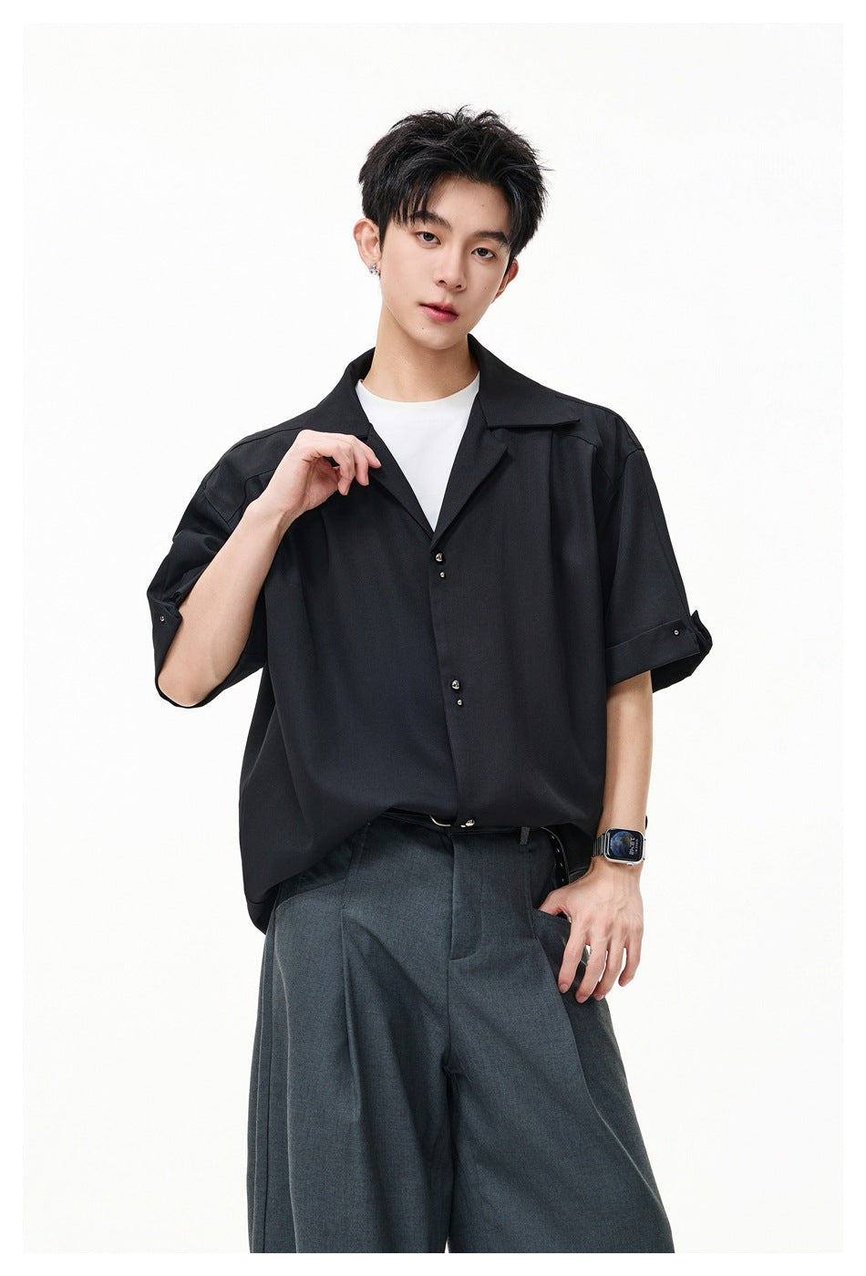 Man in black oversized short-sleeve shirt with open collar, white tee underneath and gray wide-leg pants