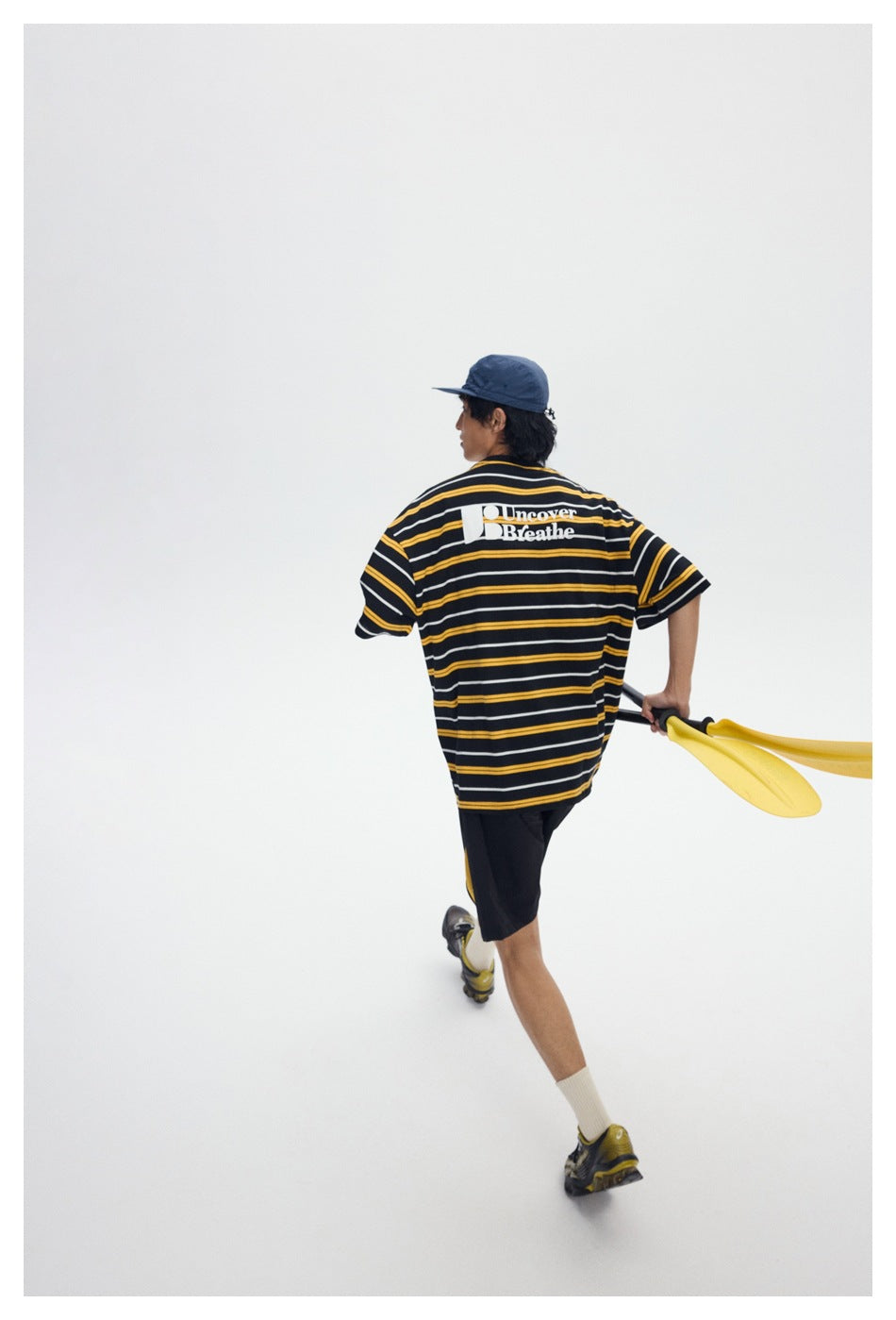 Rear view of a model wearing a black T-shirt with yellow and white stripes and a white back graphic.