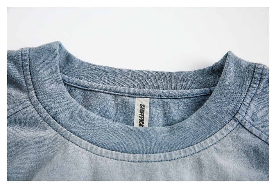 Close-up of the faded blue shirt's ribbed crew neck, shoulder seams, and sewn-in label.