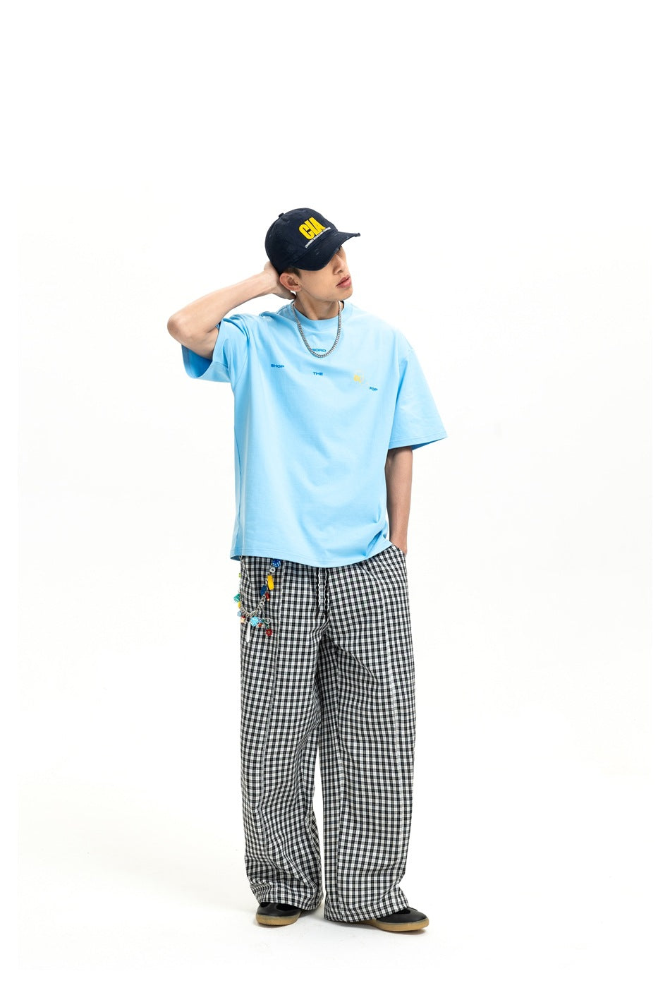Model wearing a light blue oversized graphic T-shirt with black-and-white check trousers, shown full length.