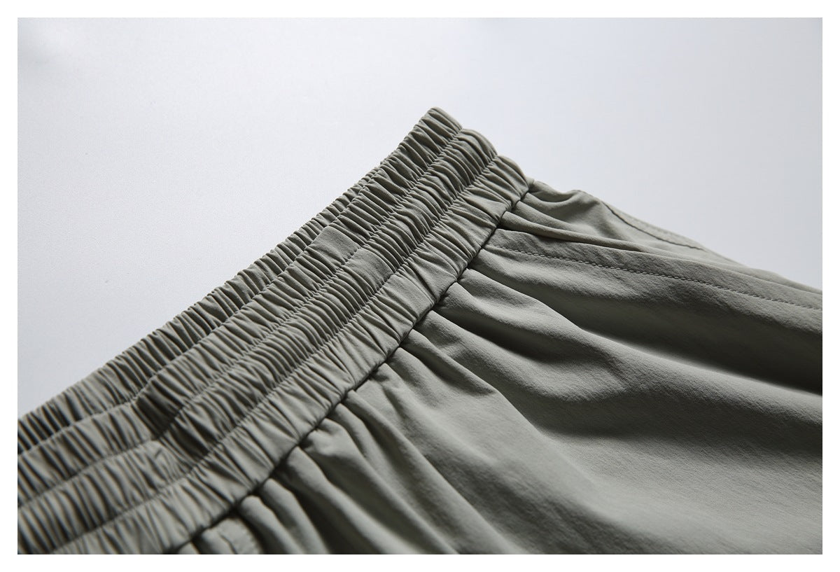 Close-up of the gathered elastic waistband and seams on gray-green shorts.