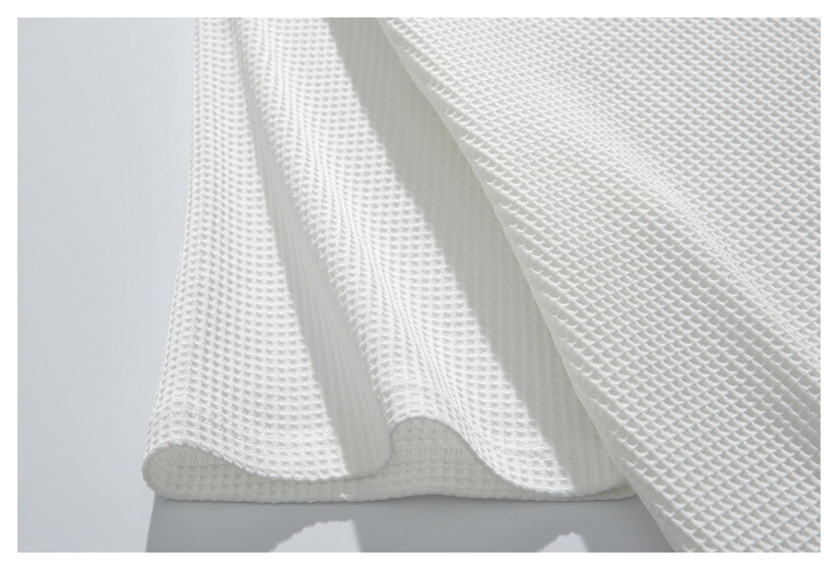 Close-up of white waffle-textured fabric draped to show a folded edge and stitched hem.