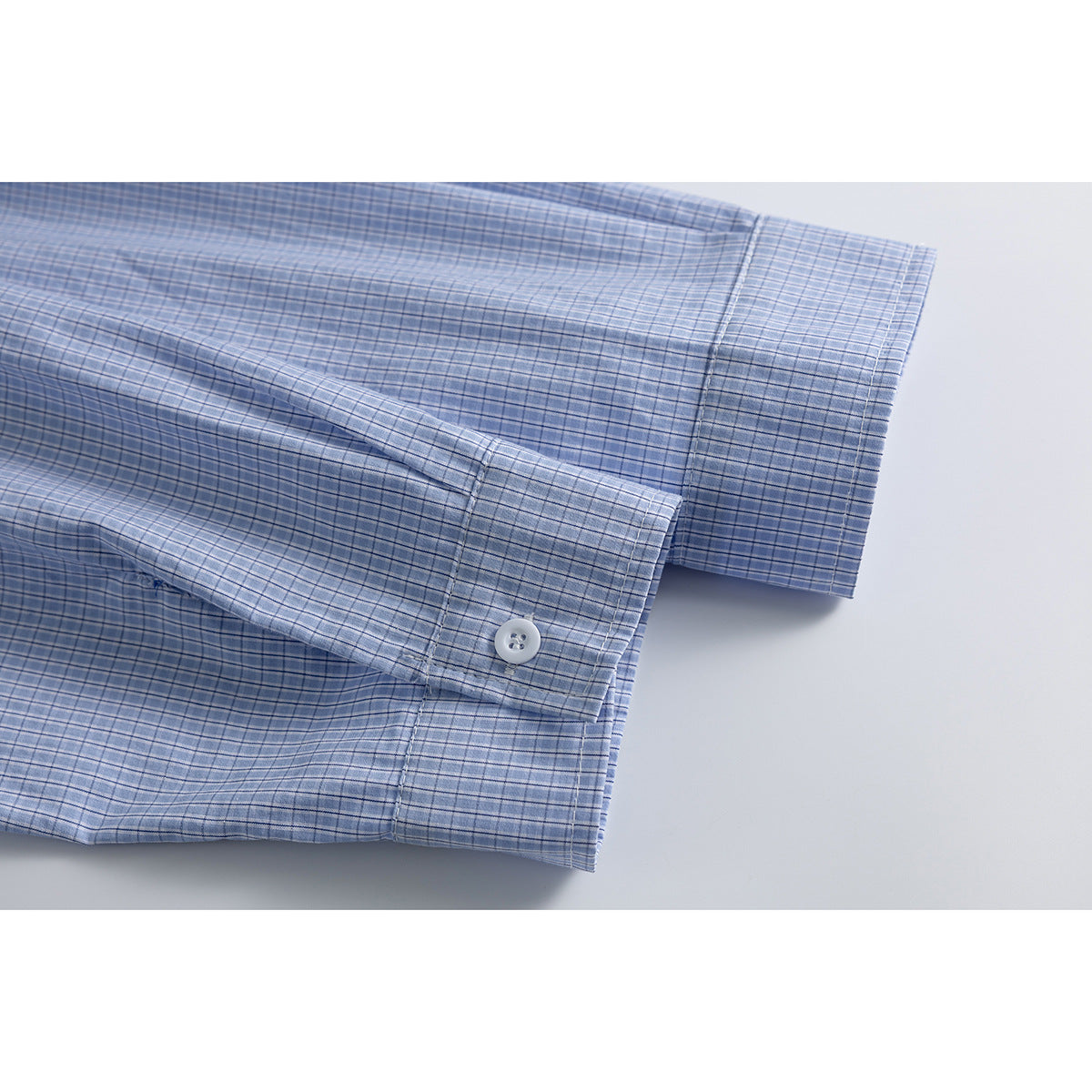 Close-up of the light blue checked shirt's buttoned cuff and sleeve.