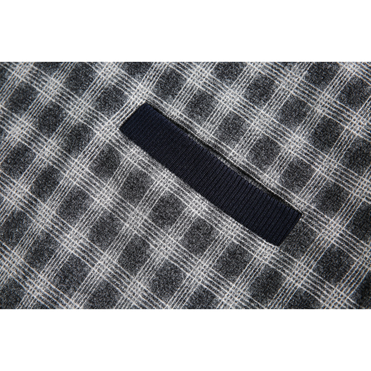 Close-up of a dark navy ribbed-trim pocket opening on gray plaid fabric.
