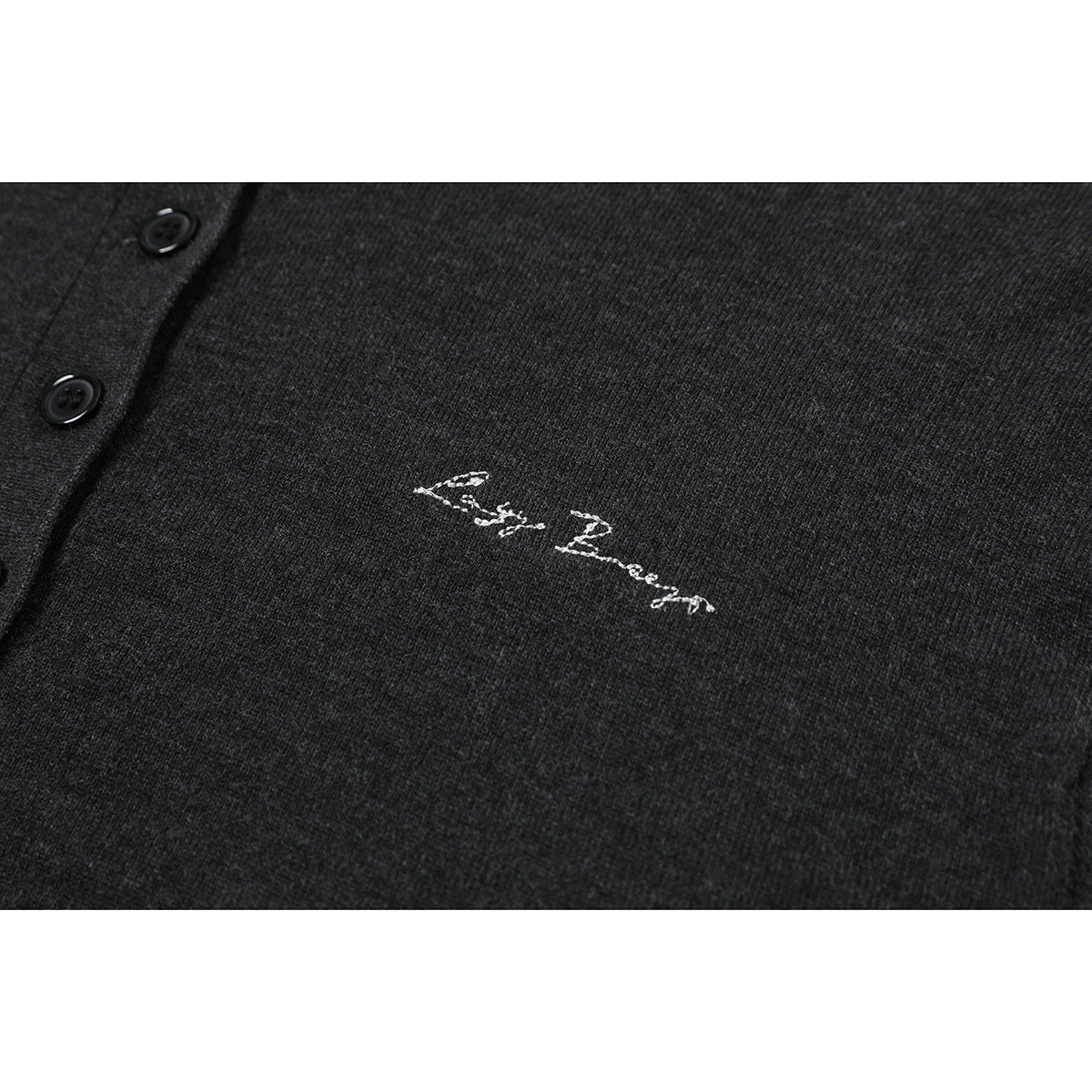 Close-up of white cursive embroidery on charcoal knit fabric beside black buttons.