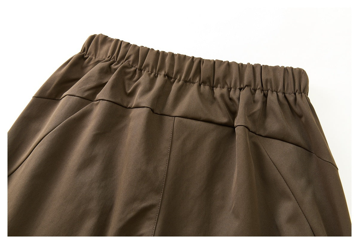 Close-up of the back of brown trousers showing a gathered elastic waistband and panel seams.