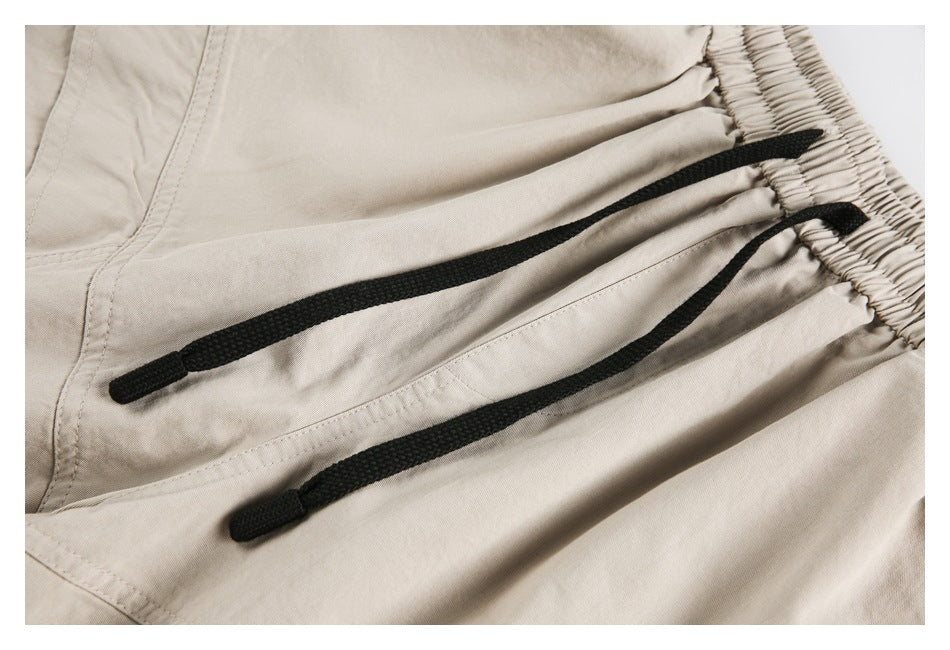 Close-up of beige pants showing two black drawstrings emerging from a gathered elastic waistband.