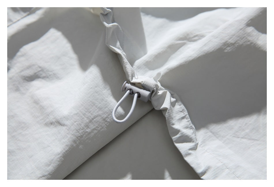Close-up of pale gray fabric gathered around a white drawcord toggle.