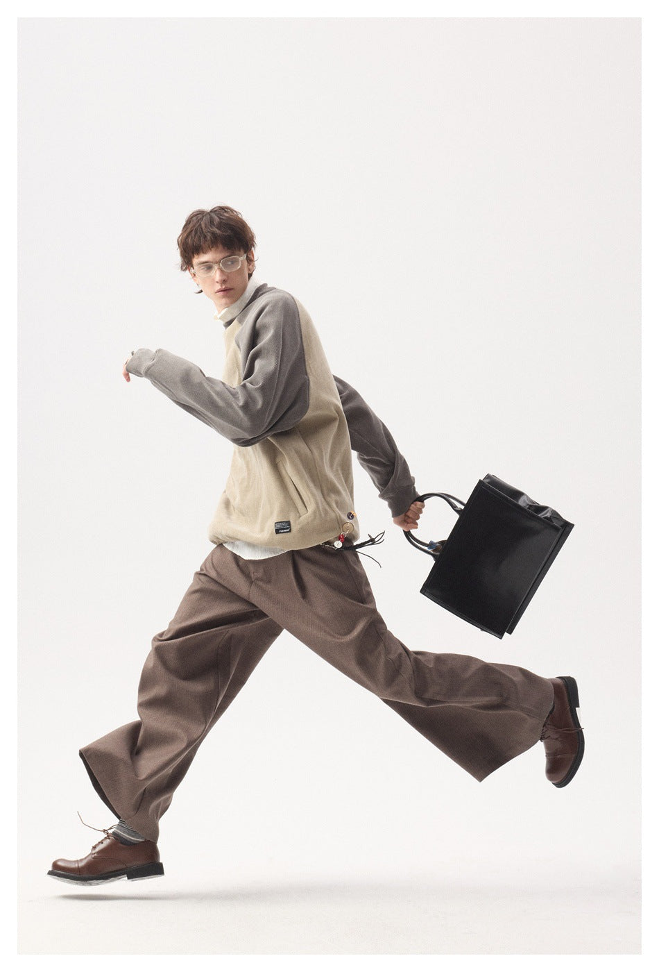 Model wearing a beige pullover with gray raglan sleeves and brown wide-leg trousers, shown in motion.