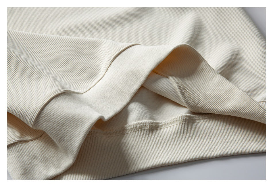 Close-up of cream waffle-knit fabric and a wide ribbed edge with visible stitching.