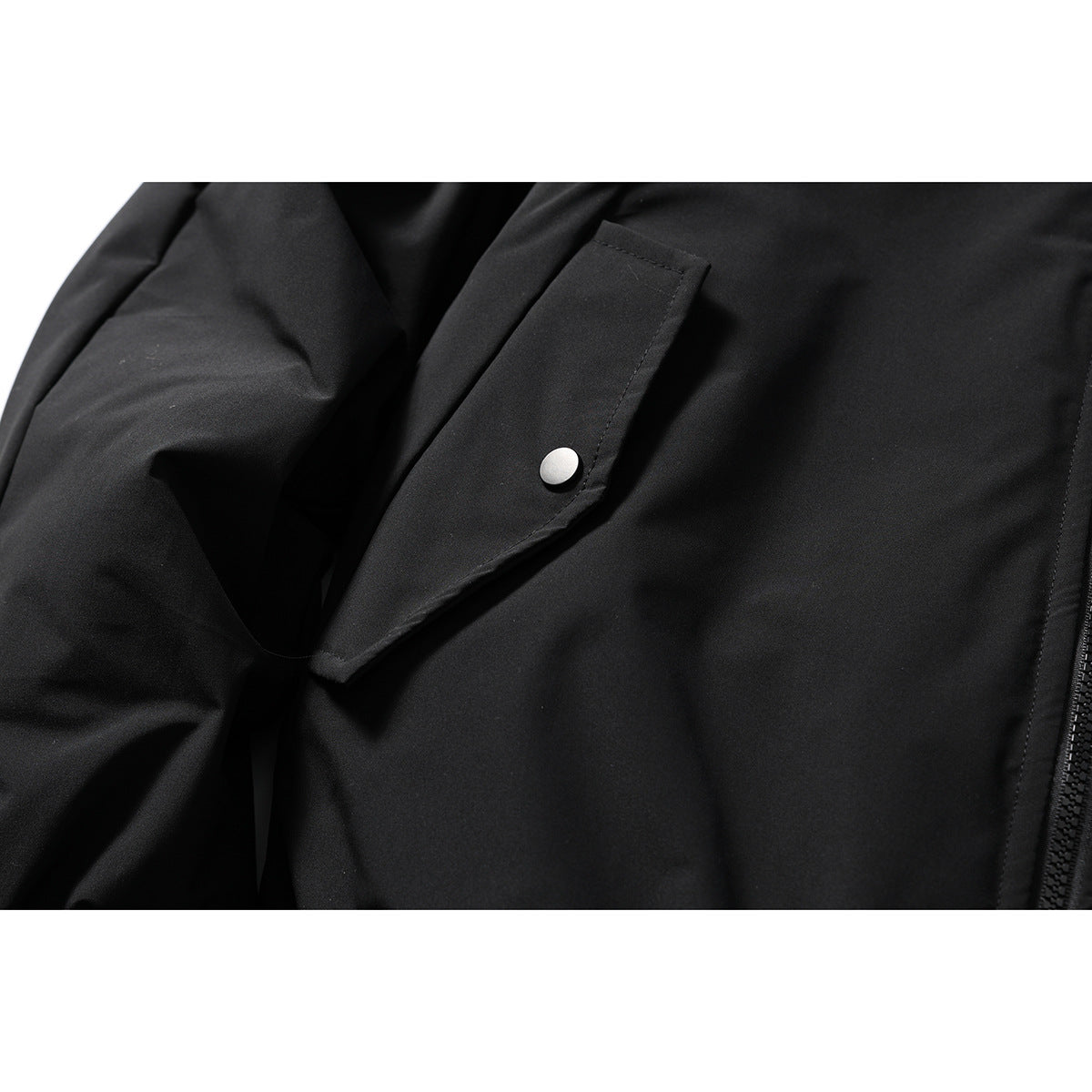 Close-up of a black jacket's angled pocket flap with a silver snap button and the edge of its zipper.