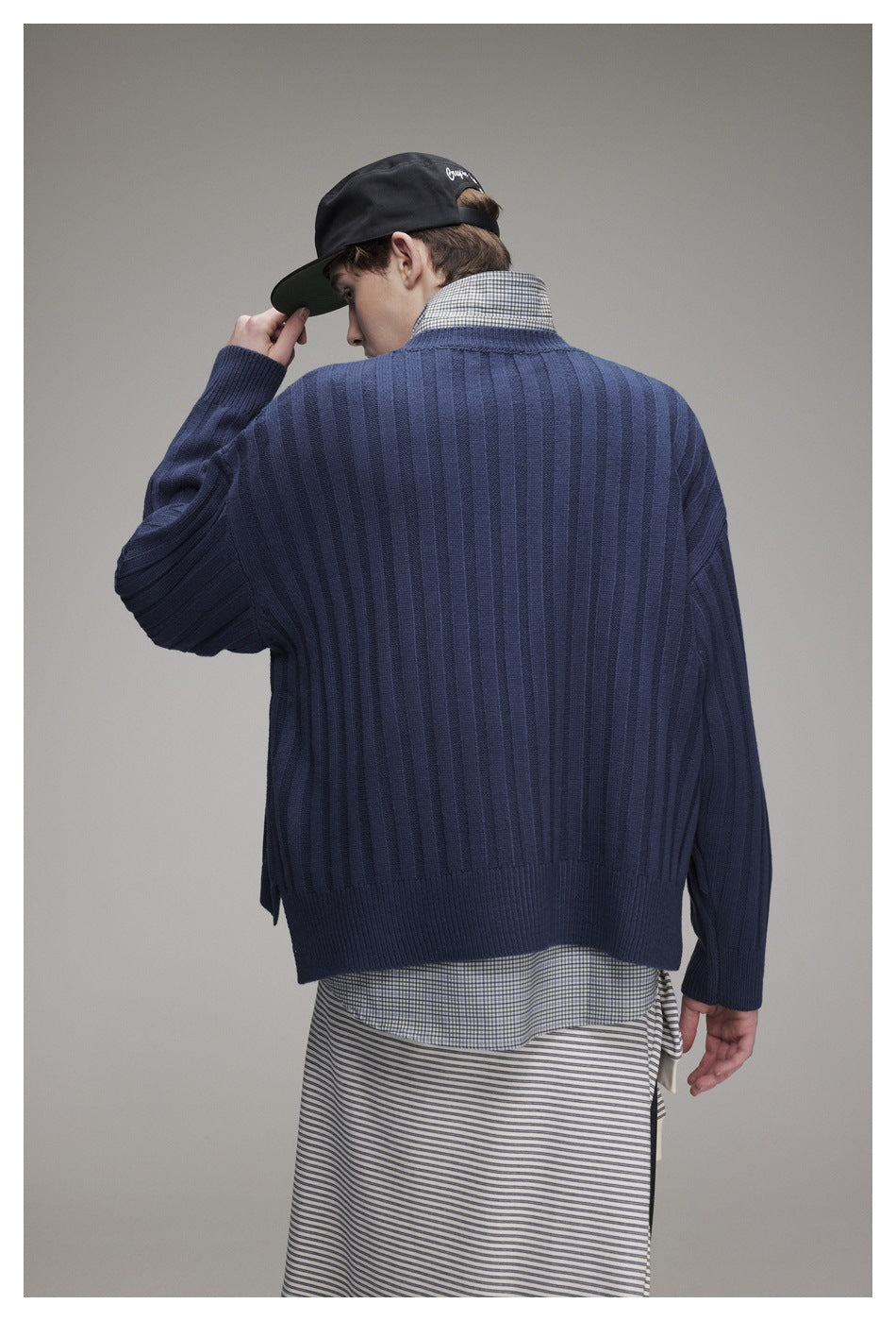 Back view of a model wearing a loose navy rib-knit sweater over a checked shirt.