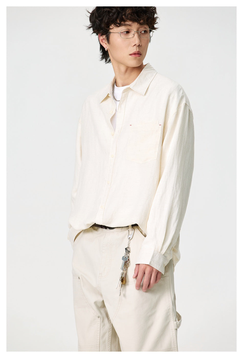 Model wearing an ivory button-up shirt with a chest pocket and matching utility-style trousers.