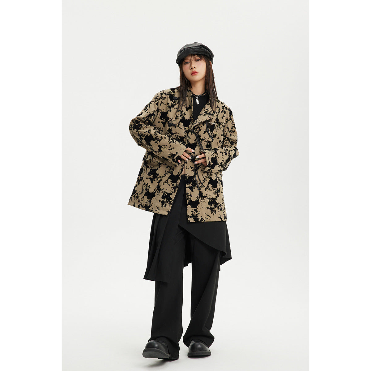 Model wearing a tan jacket with a bold black abstract pattern and toggle closures, styled with black layers.
