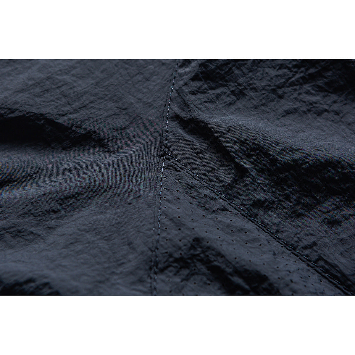 Close-up of dark jacket fabric with stitched panels and a perforated section.