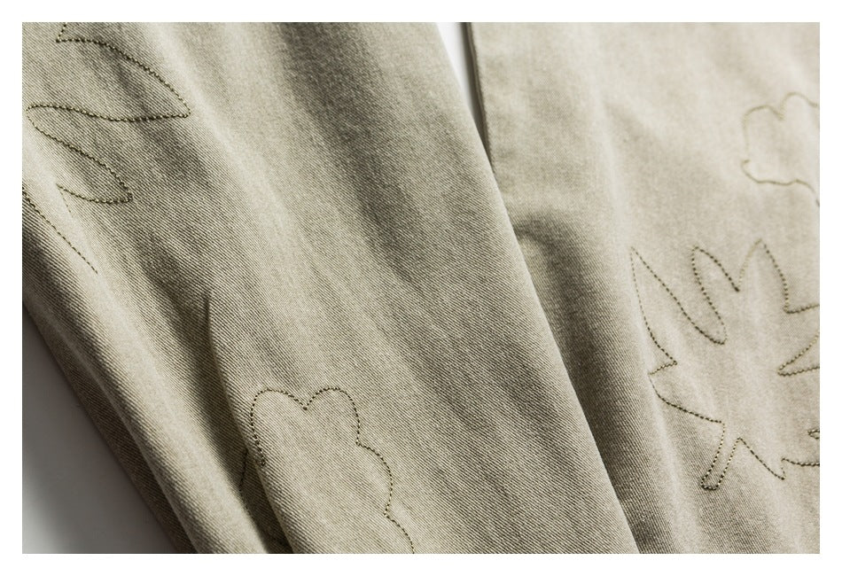 Close-up of khaki-olive fabric with outlined leaf stitching on the sleeve and body.
