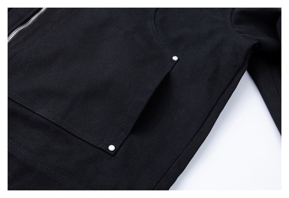 Close-up of a black jacket's stitched front pocket with two silver snap fasteners.