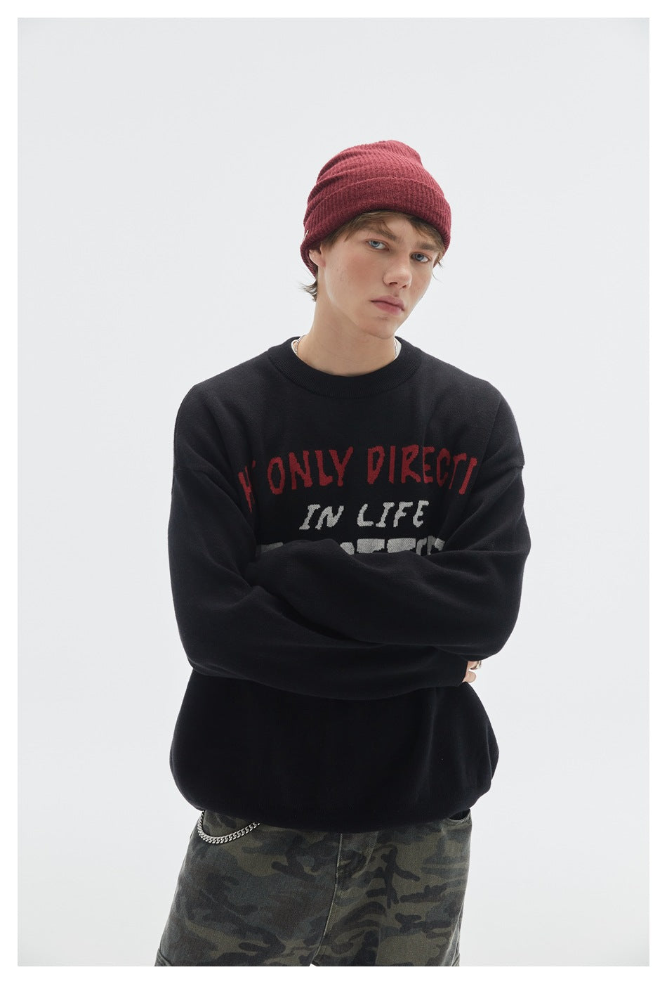Close view of a model in a black crewneck sweater with red and white lettering and a burgundy beanie.