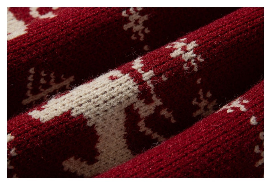 Macro view of cream reindeer and snowflake motifs knitted into deep red fabric.