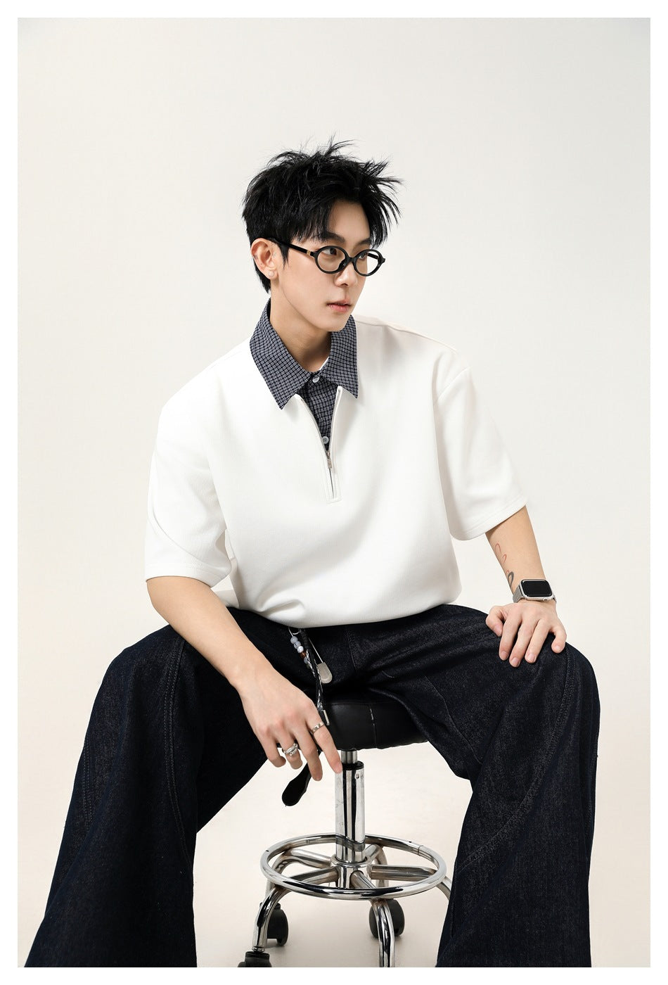 Seated model wearing a white short-sleeve quarter-zip polo with a checked collar.
