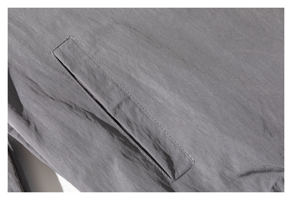 Close-up of a slanted welt pocket stitched onto gray jacket fabric.