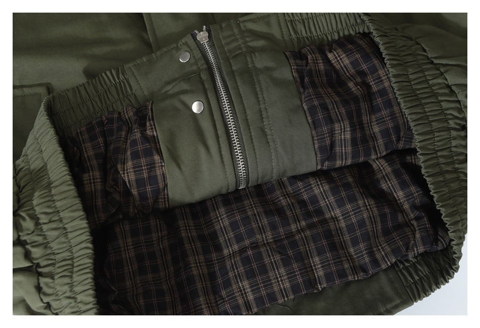 Open olive jacket showing dark plaid lining, a metal zipper, snap buttons, and gathered trim.