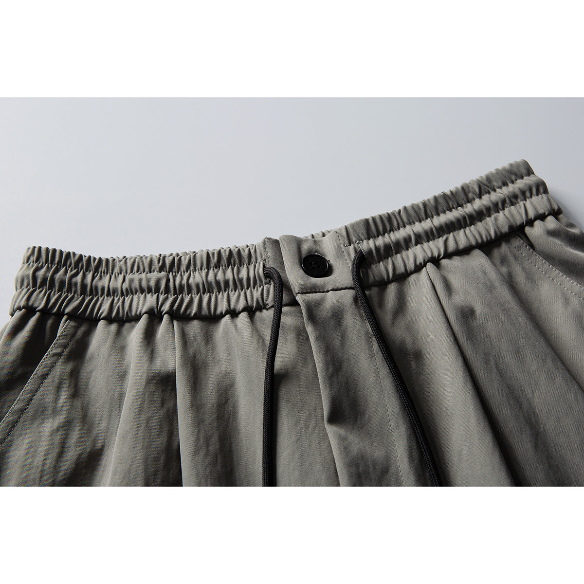 Close-up of gray trousers showing an elastic waistband, black button, drawstrings, and front pleats.